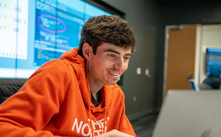 Data analytics student smiling and looking at laptop