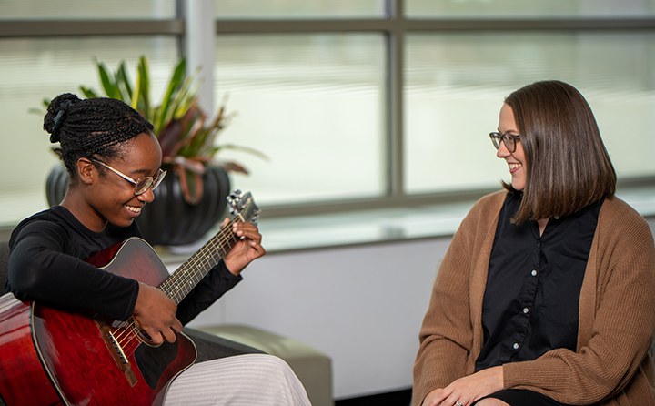 music therapy student playing guitar next to professor