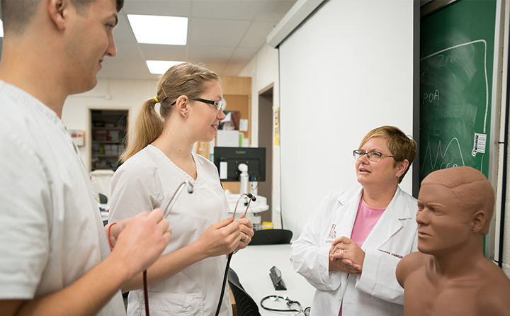 Two nursing students talk with professor