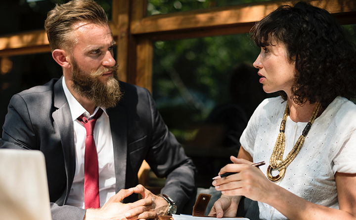 Photo of two people in business attire talking outside at a table
