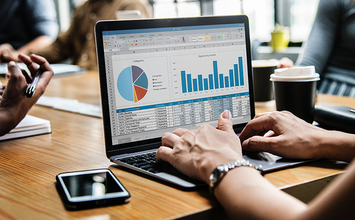 Photo of person typing on a laptop with business graphs on the screen