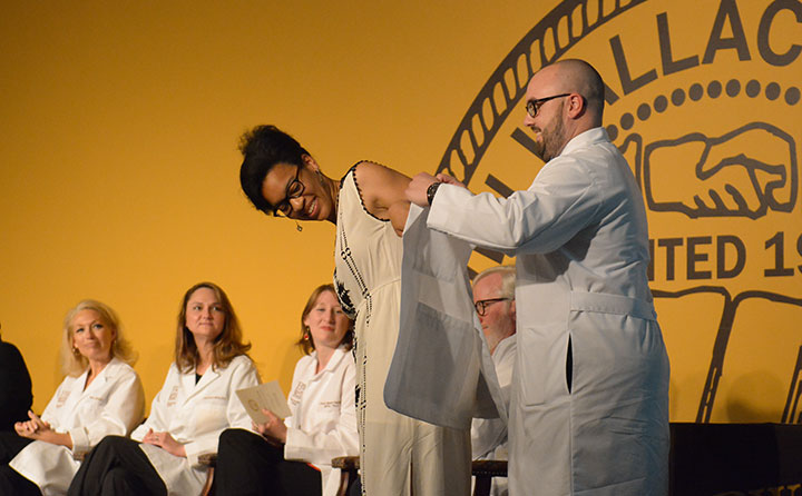PA department chair Jared Pennington helps second-year student Joy Akuchie slip into a medical jacket and mark a milestone during the program's 2016 White Coat Ceremony.