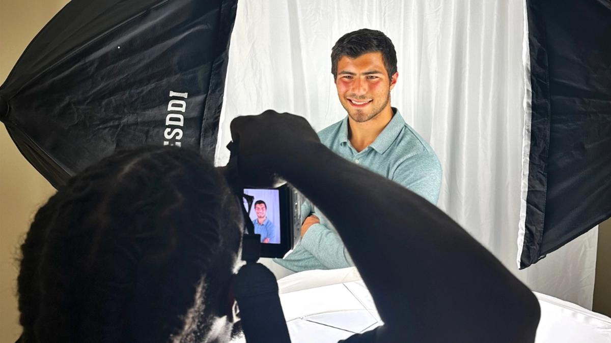 Student photographer taking professional headshots of other students, with individuals posing while others wait or prepare in a campus setting.